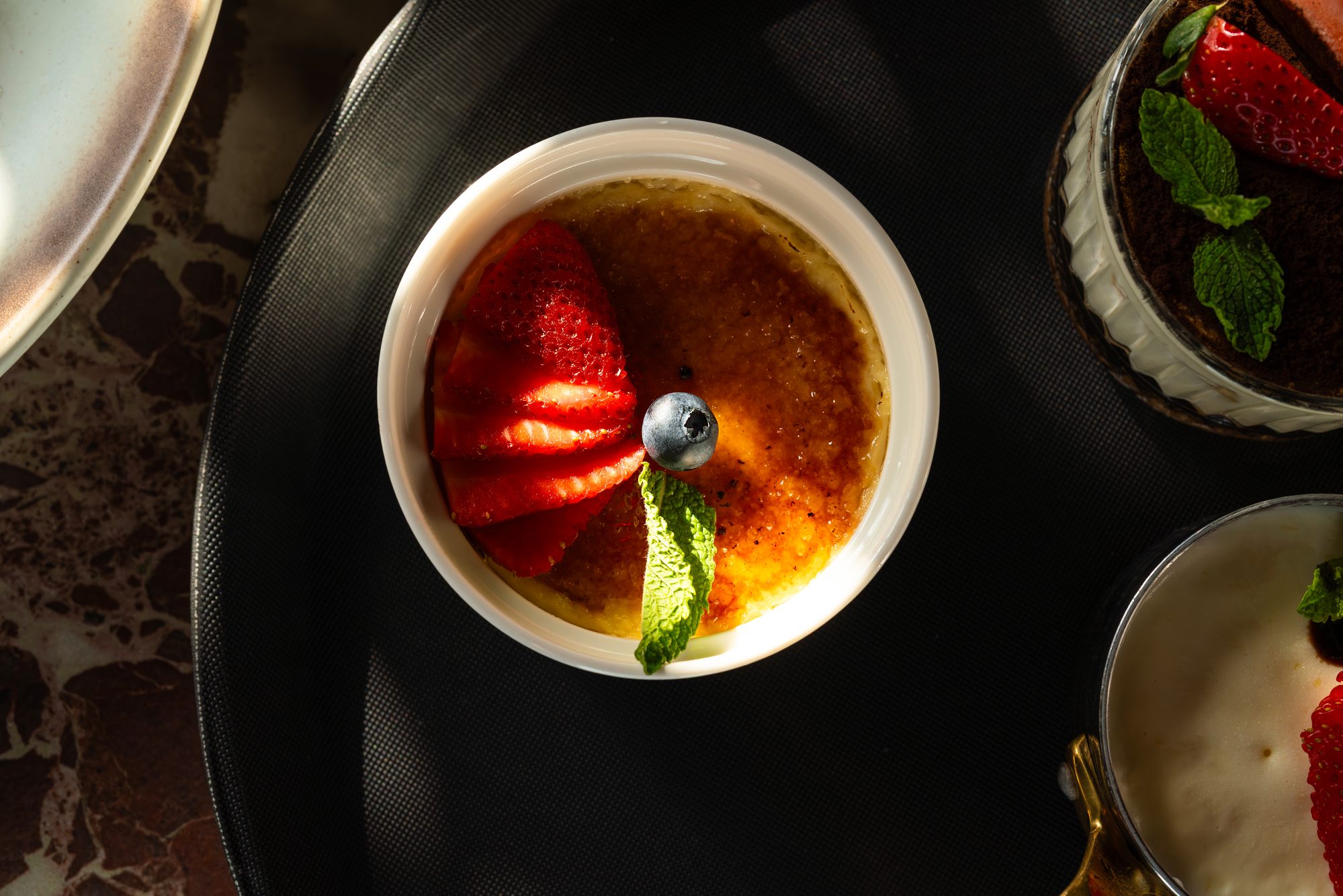 Crème brûlée with strawberries and mint, photographed from above on dark cloth